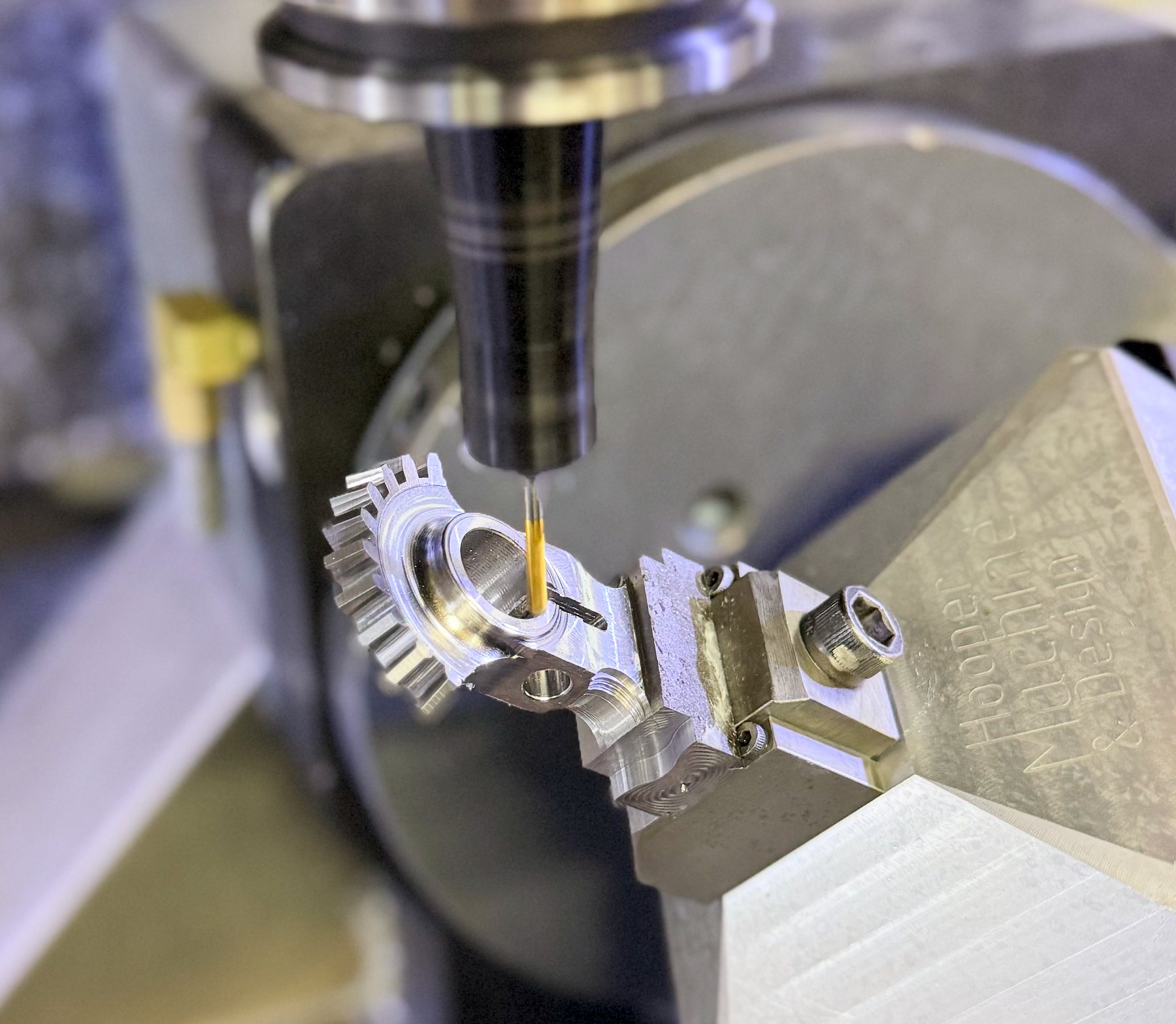 Gold-coated end mill cutting a replacement gear for a 100-year-old Buick, held in a fixture engraved Hooper Machine & Design on the 5-axis trunnion